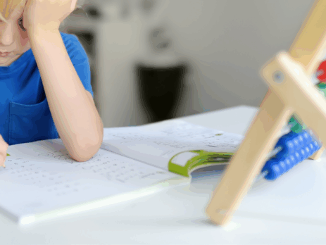 Enfant assis à un bureau, concentré sur un exercice écrit, montrant des signes de difficulté d’attention lors d’une activité scolaire.