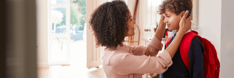 Une mère ajuste délicatement le sac d’école de son jeune fils dans l’entrée ensoleillée de la maison avant le retour en classe.