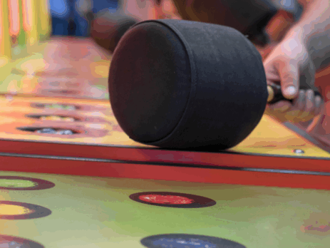 Main tenant un gros marteau rembourré au-dessus des trous colorés d’un jeu de foire où il faut frapper les marmottes qui apparaissent.