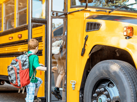 Enfant portant un sac à dos montant dans un autobus scolaire jaune par une matinée ensoleillée.