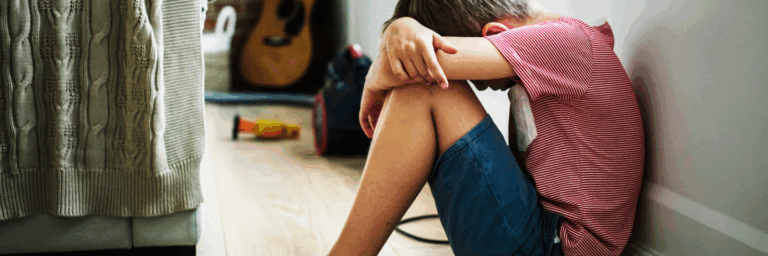 Enfant assis au sol, la tête appuyée sur ses bras, exprimant un moment de détresse ou de peur dans un environnement familial.