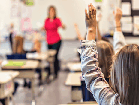 « Des élèves en classe levant la main pendant qu’une enseignante donne un cours, illustrant l’énergie et les ajustements liés au retour en classe.