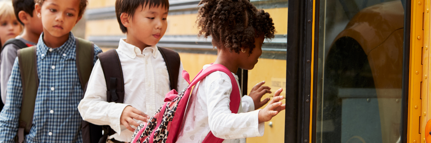 Groupe d’enfants portant des sacs à dos qui montent à bord d’un autobus scolaire jaune.