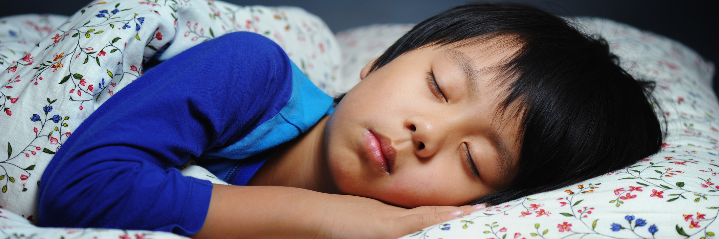 « Enfant endormi paisiblement dans son lit, la tête appuyée sur une taie d’oreiller fleurie.