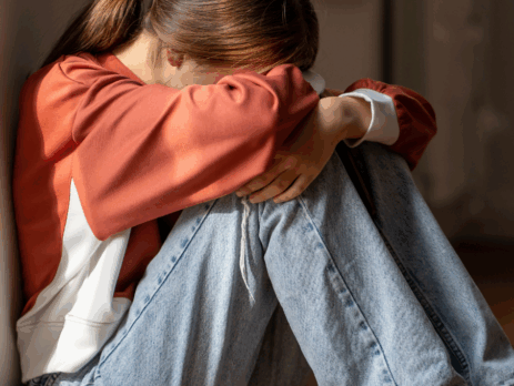 Enfant assis au sol, recroquevillé contre un mur, les bras entourant ses genoux, exprimant un état de détresse émotionnelle ou d’anxiété.