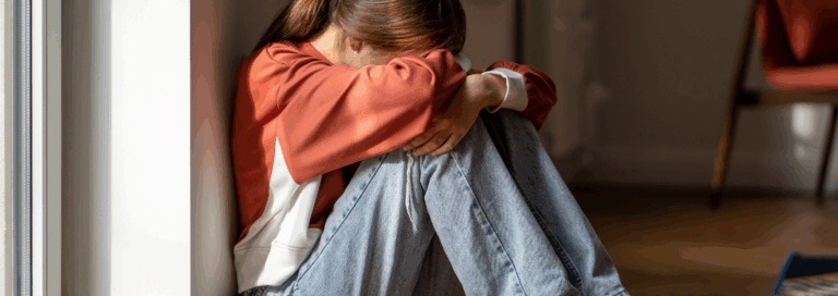 Enfant assis au sol, recroquevillé contre un mur, les bras entourant ses genoux, exprimant un état de détresse émotionnelle ou d’anxiété.