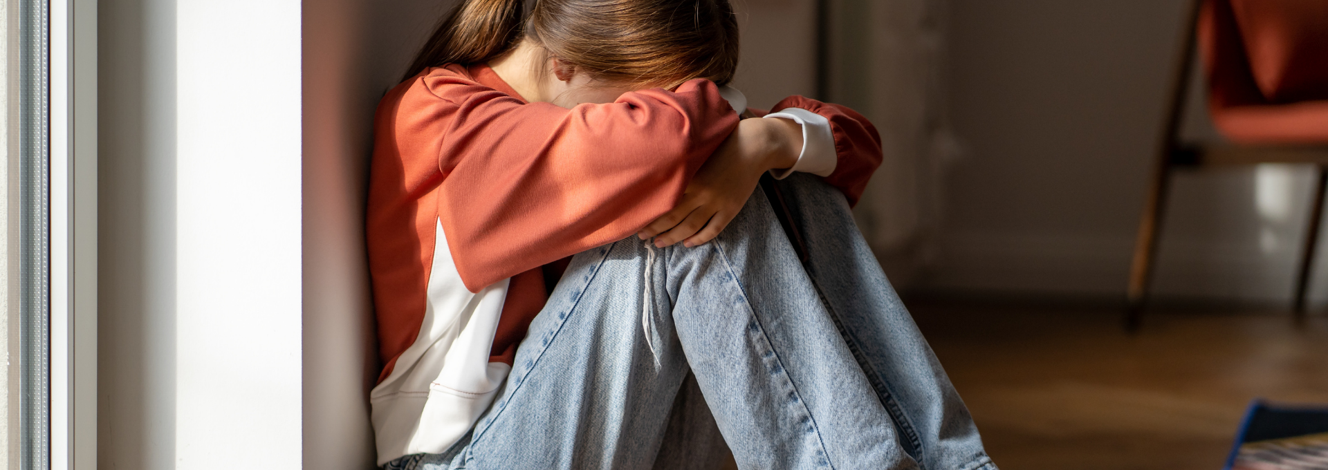 Enfant assis au sol, recroquevillé contre un mur, les bras entourant ses genoux, exprimant un état de détresse émotionnelle ou d’anxiété.